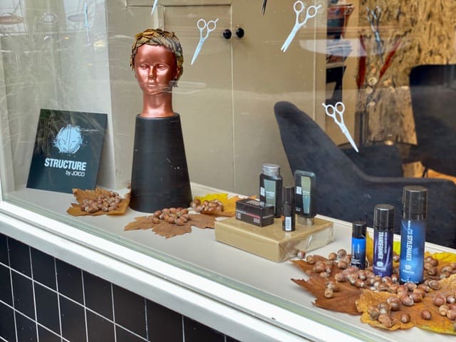 Etalage met een paspop, haarproducten en najaarsblad achter het glas
